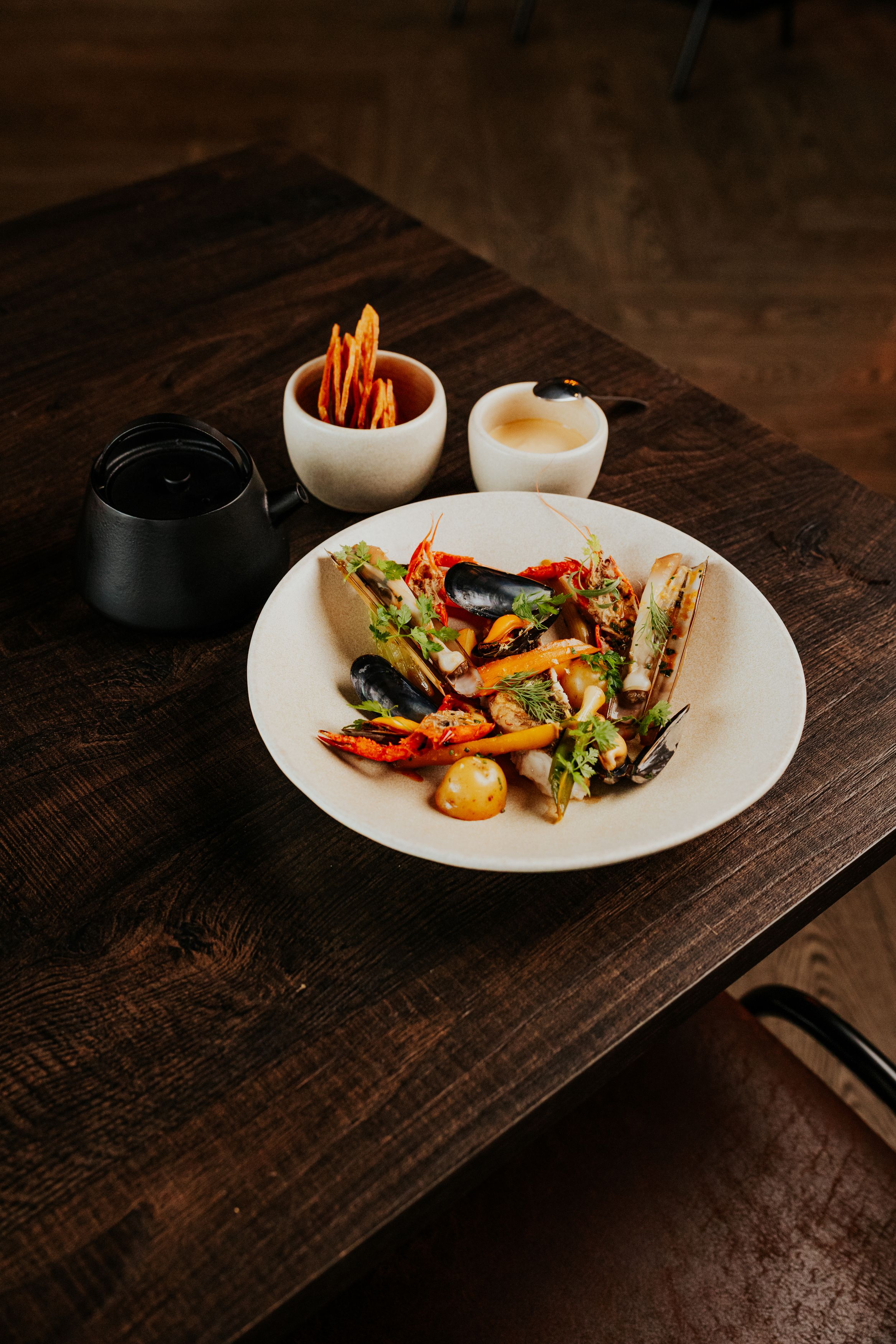Elegant seafood dish with colorful vegetables served on white plate against dark wooden table.