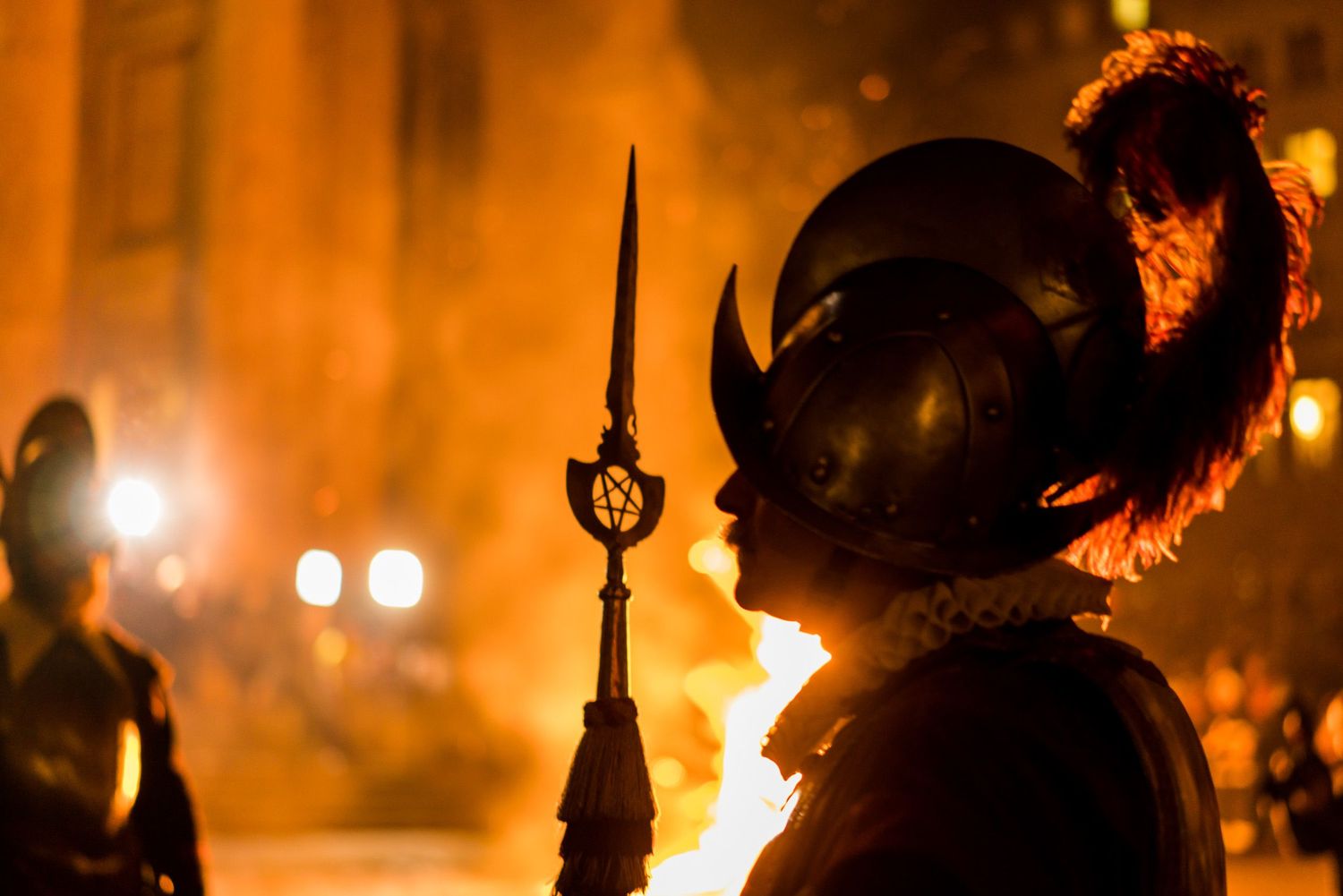 People march through city streets at night carrying lit torches and creating an illuminated procession.