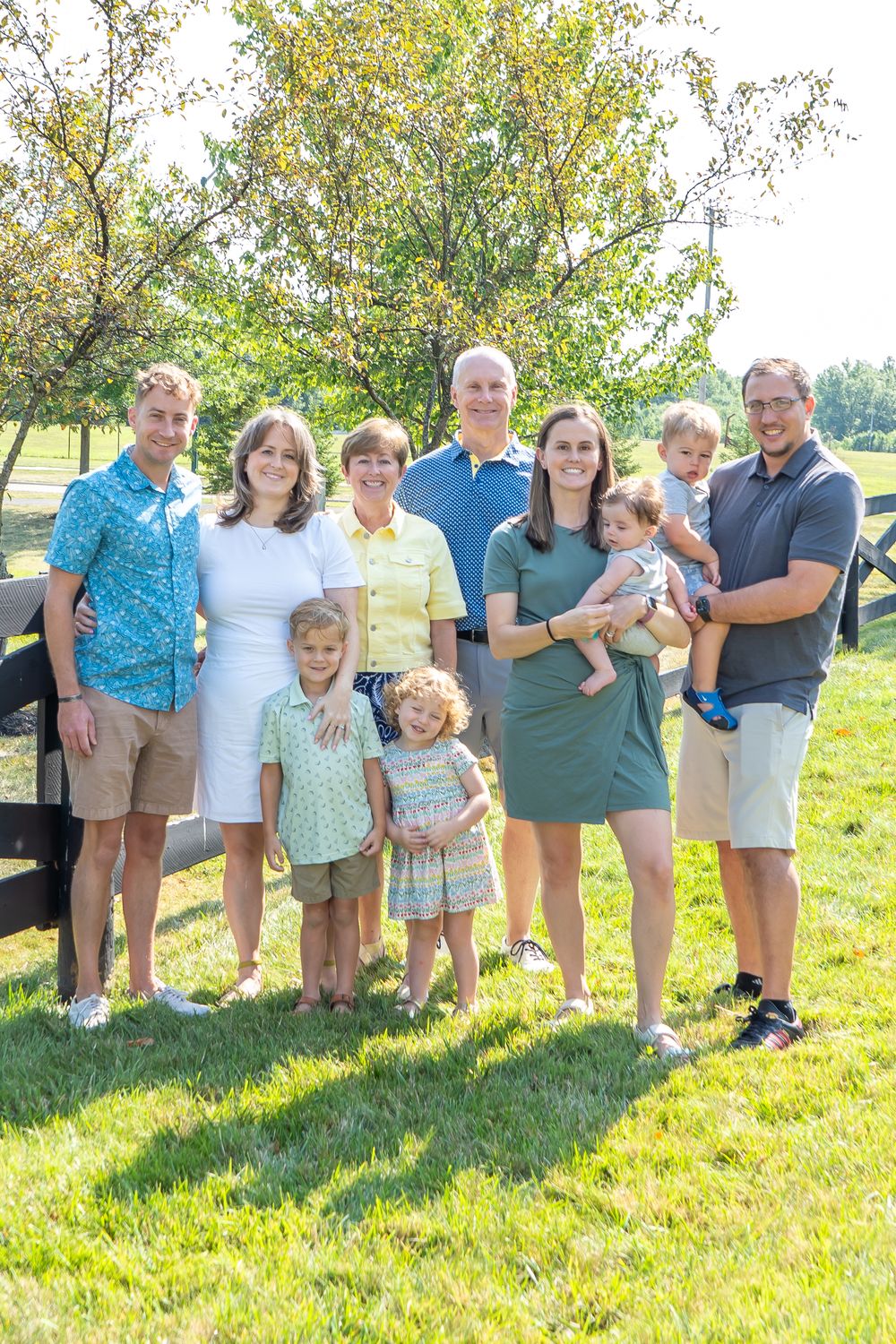 Extended family group poses together on a sunny grassy hillside during a summer gathering.