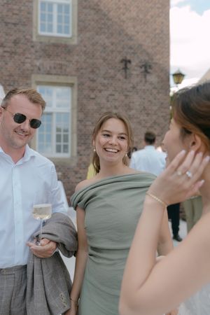 Guests in summer attire enjoying cocktails at an outdoor wedding reception by a brick building.