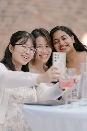 Friends taking a selfie together while enjoying drinks at an outdoor wedding reception.