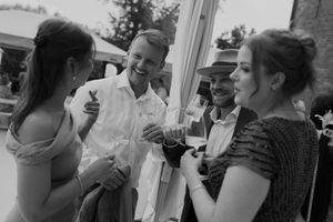Wedding guests sharing drinks and conversation at an outdoor reception in black and white.