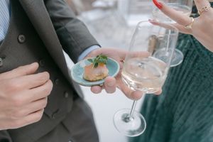 Close-up of hands holding wine glasses and appetizer plates at an elegant reception.