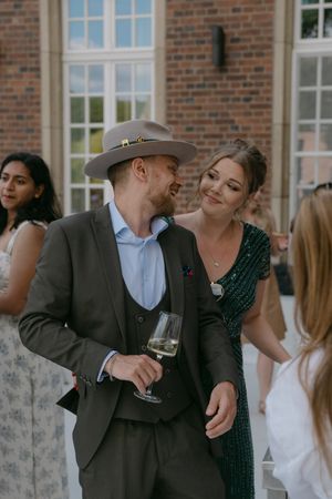Guests share joyful moments at an outdoor wedding reception near a brick building.