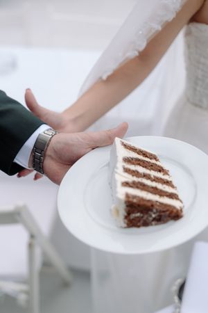 Slice of layered white wedding cake being served on elegant white plate.