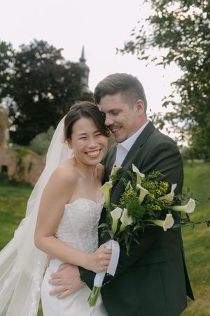 Couple embraces while holding elegant white calla lily bouquet in garden setting.