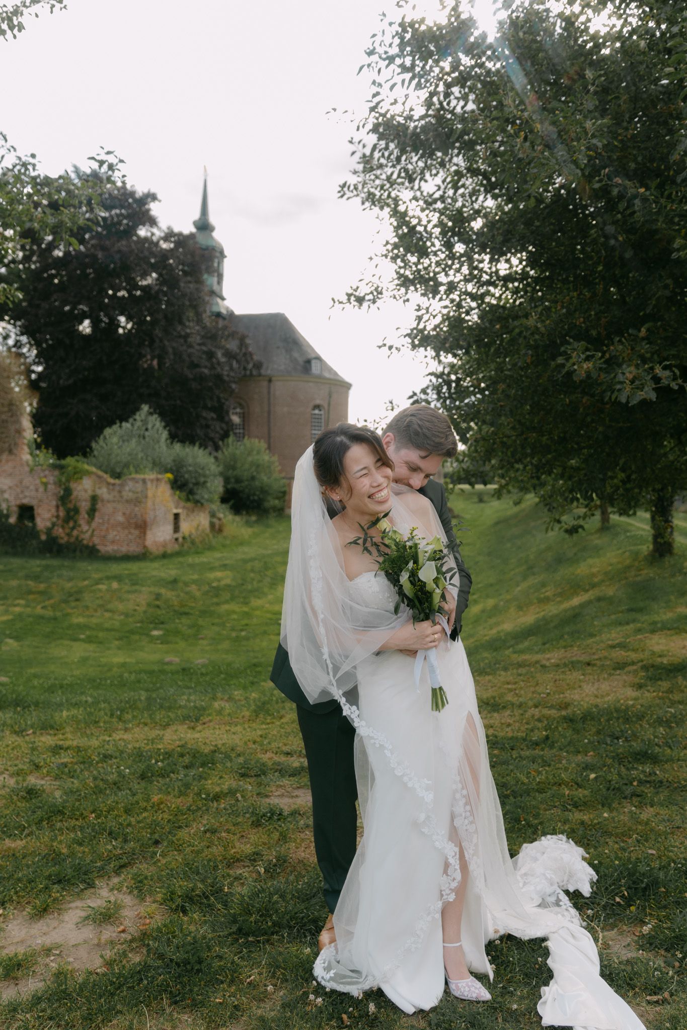 Romantic wedding moment captured between a couple on a grassy hill with historic buildings in the background.