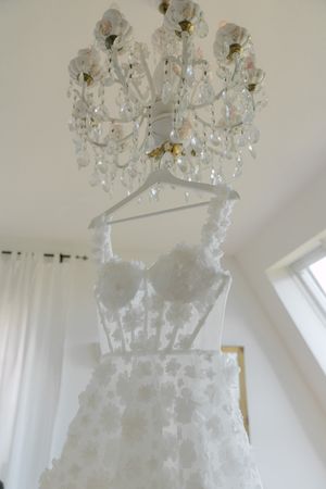Crystal chandelier illuminating an elegant white wedding dress in a bright room.