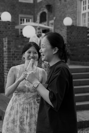Black and white photo of wedding guests sharing drinks and laughter at an outdoor celebration.