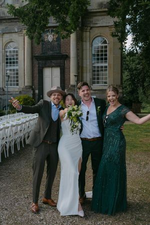 Wedding party poses together for a group photo outside a historic building with white chairs in the background.