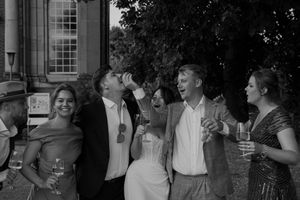 Wedding party laughs together during outdoor celebration at historic venue.