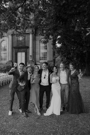 Group photo of wedding party lined up on grass in front of brick building.