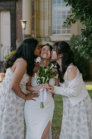 Bridesmaids in floral dresses share emotional embraces with bride outside.