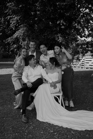 Wedding party poses playfully on the grass in black and white photo with bride's white dress flowing.