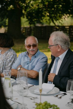 Elderly guests in formal attire engaged in conversation at an outdoor wedding reception.