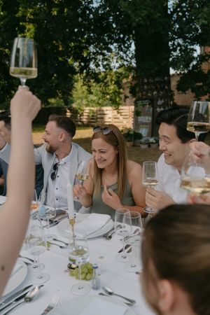 Wedding guests in formal attire laughing and celebrating at an outdoor reception table.