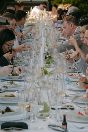 Long dining table filled with guests enjoying a formal meal with white tablecloths and glassware.