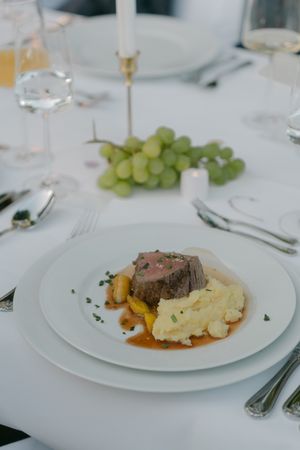 Plated gourmet meals with meat and sides served on white dishes at a formal dinner.