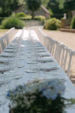Long white dining table set for an elegant outdoor wedding reception with floral centerpieces.