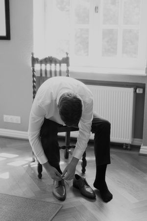 Person in white shirt and dark pants bending over to search on wooden floor.