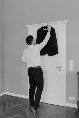 Person hanging up a dark suit jacket on white door in minimalist room.