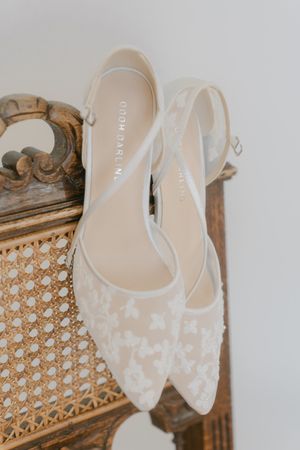 Delicate white lace bridal shoes displayed on vintage wooden furniture.