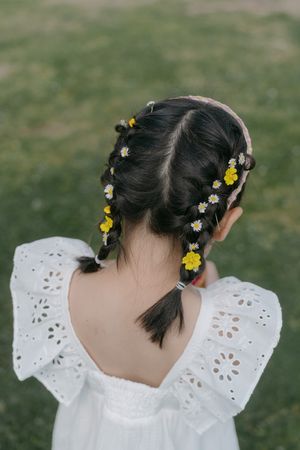 Back view of an intricate braided hairstyle adorned with small yellow flowers and white eyelet dress.