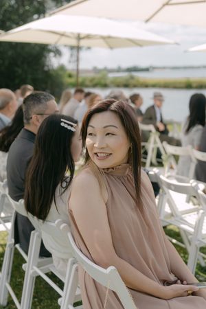 Outdoor wedding ceremony seating with white chairs and umbrellas overlooking waterfront.