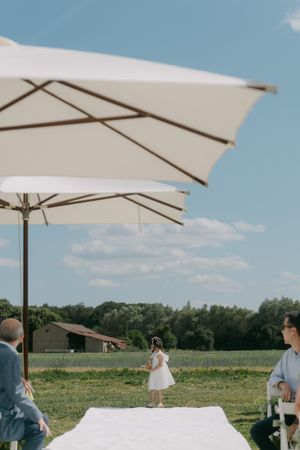 White umbrella canopies frame an outdoor wedding ceremony space with rolling hills in background.
