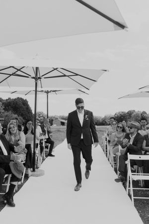 Formal procession down white aisle runner under elegant white umbrellas at outdoor ceremony.