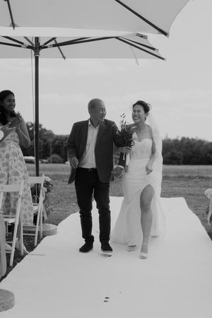 Couple walking down white aisle runner during outdoor ceremony under umbrella canopies.