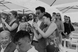 Wedding guests react emotionally during an outdoor ceremony under white umbrellas.