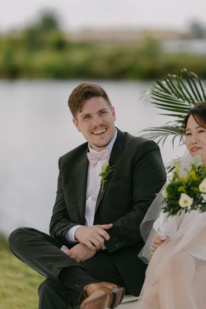 Intimate wedding ceremony moment captured by a lakeside with palm decorations.