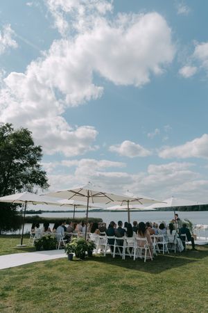 Scenic lakeside wedding setup with white umbrellas and chairs under a blue summer sky.