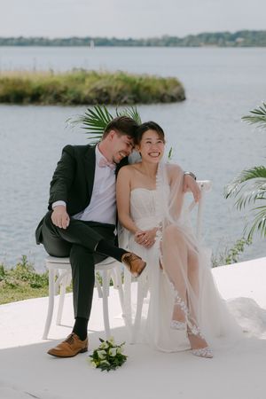 Lakeside wedding ceremony with elegant white decor and tropical palm accents.