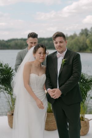 Wedding party poses together by a serene lake with decorative potted plants.