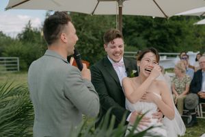 Joyful laughter shared during waterfront wedding ceremony under white umbrella.