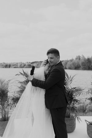 Black and white emotional embrace during waterfront wedding ceremony.