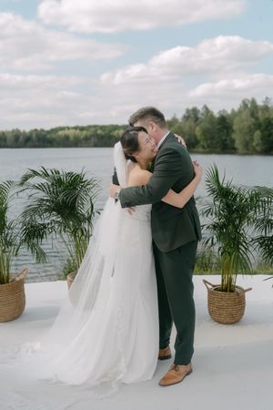 Newlyweds share first kiss as married couple during waterfront ceremony with palm decorations.