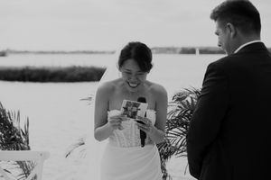 Black and white candid moment of bride reading during lakeside ceremony.