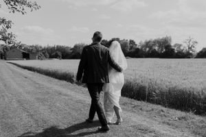 A couple walks along a countryside path in black and white, with the bride wearing a flowing white dress.