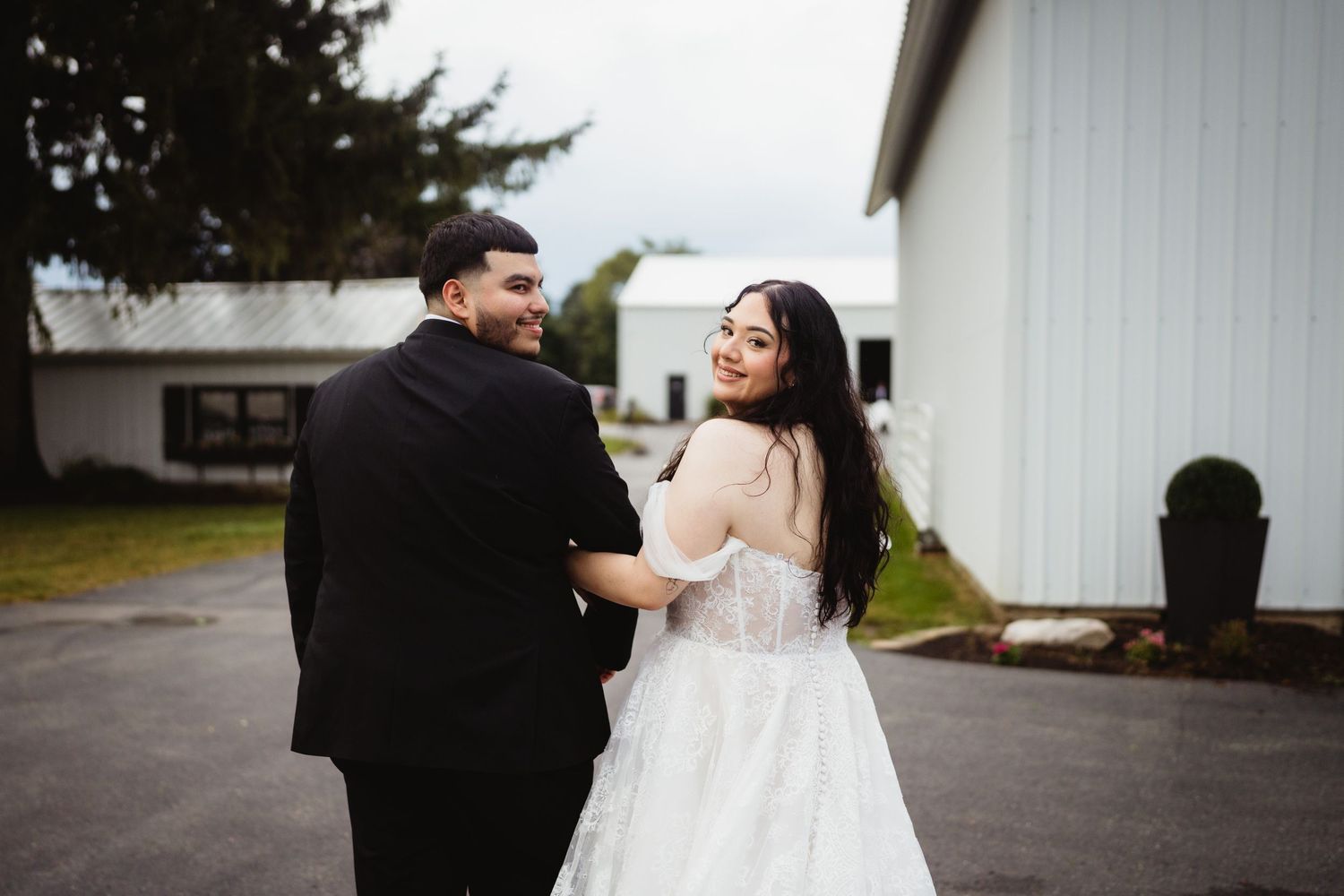 A couple in wedding attire dances and twirls together in front of a white building on their special day.