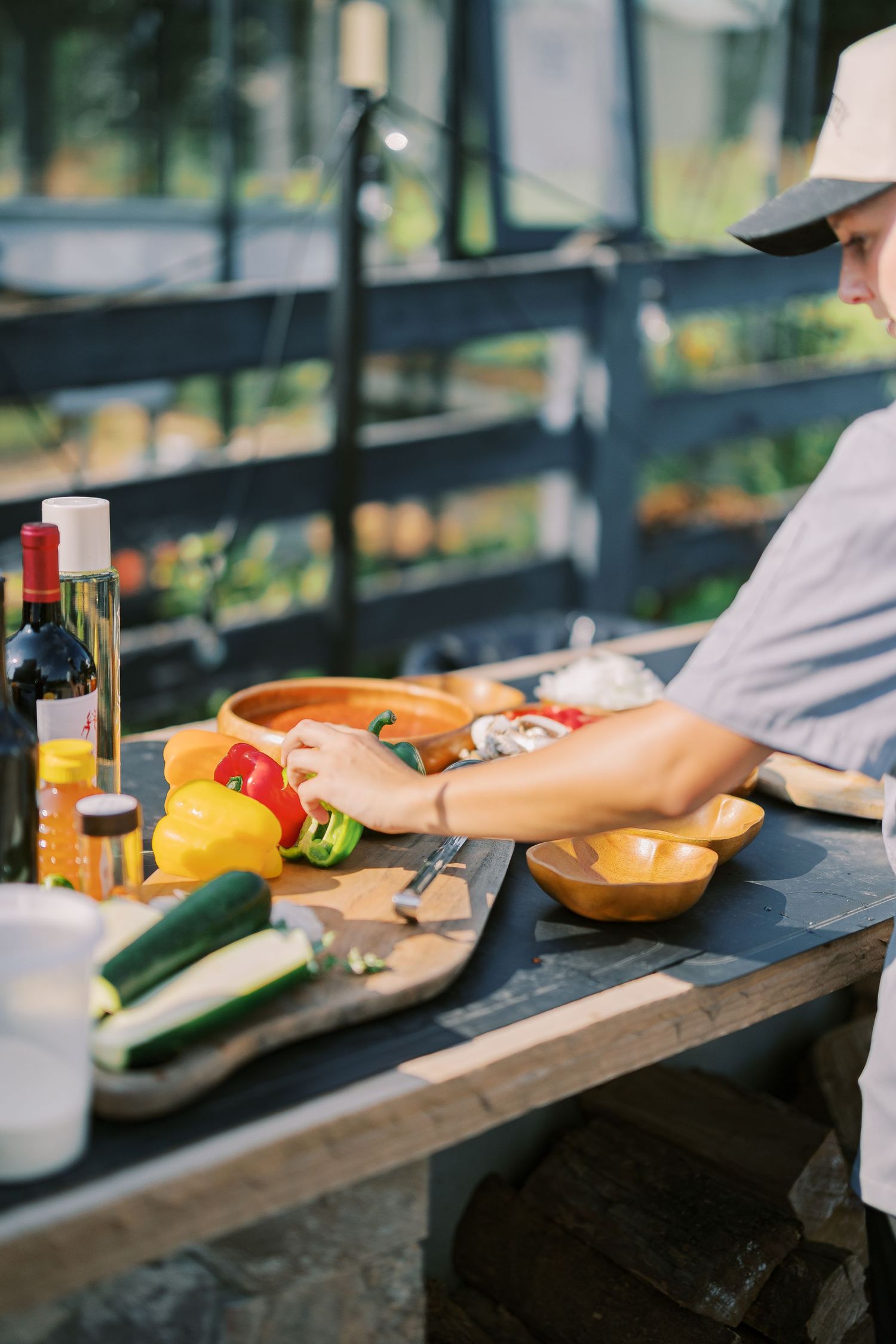 Chef in white prepares fresh ingredients on rustic wooden counter with colorful bell peppers and vegetables.