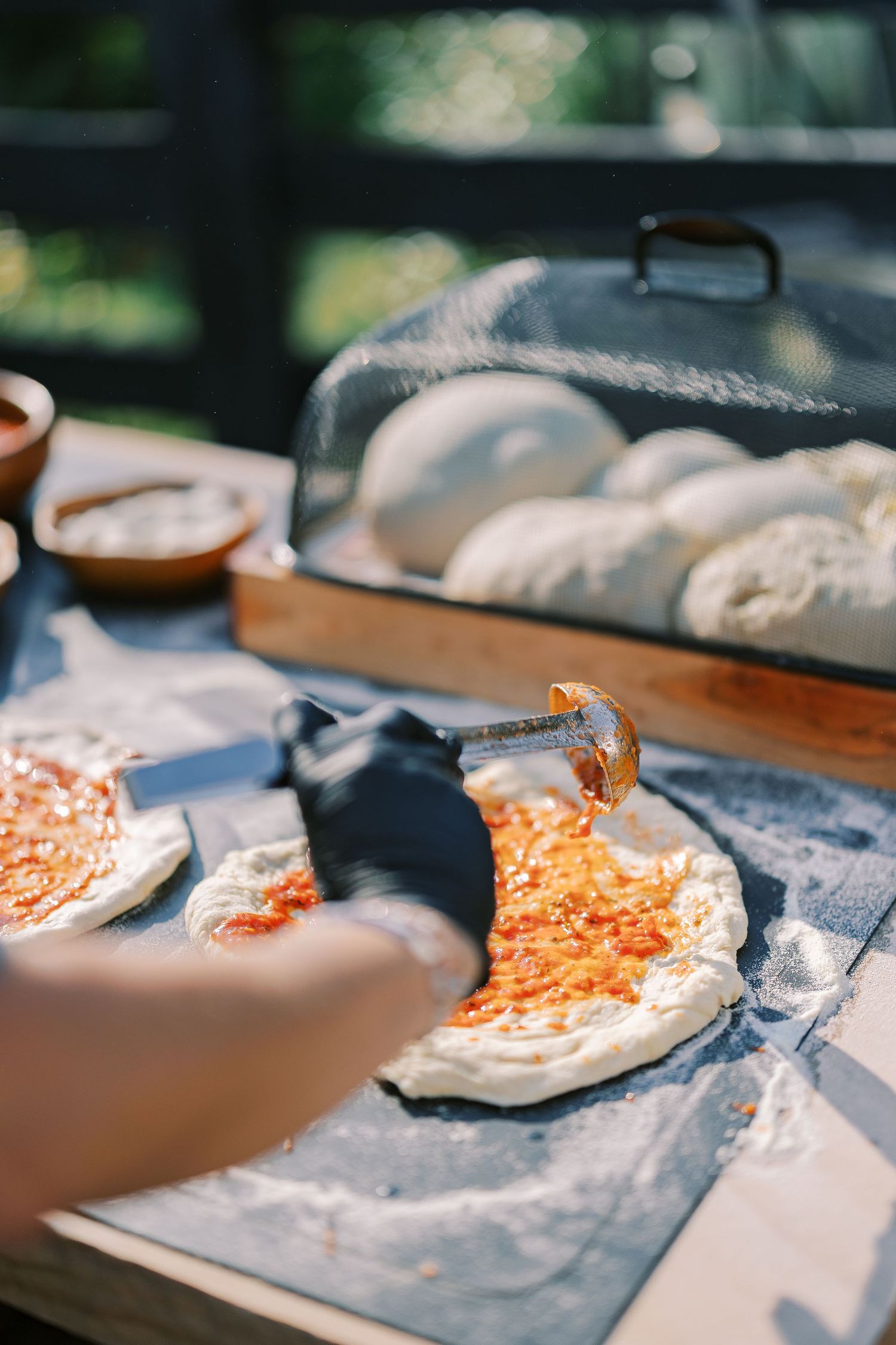 Chef rolling out pizza dough and preparing pizza bases on floured wooden surface in natural lighting.