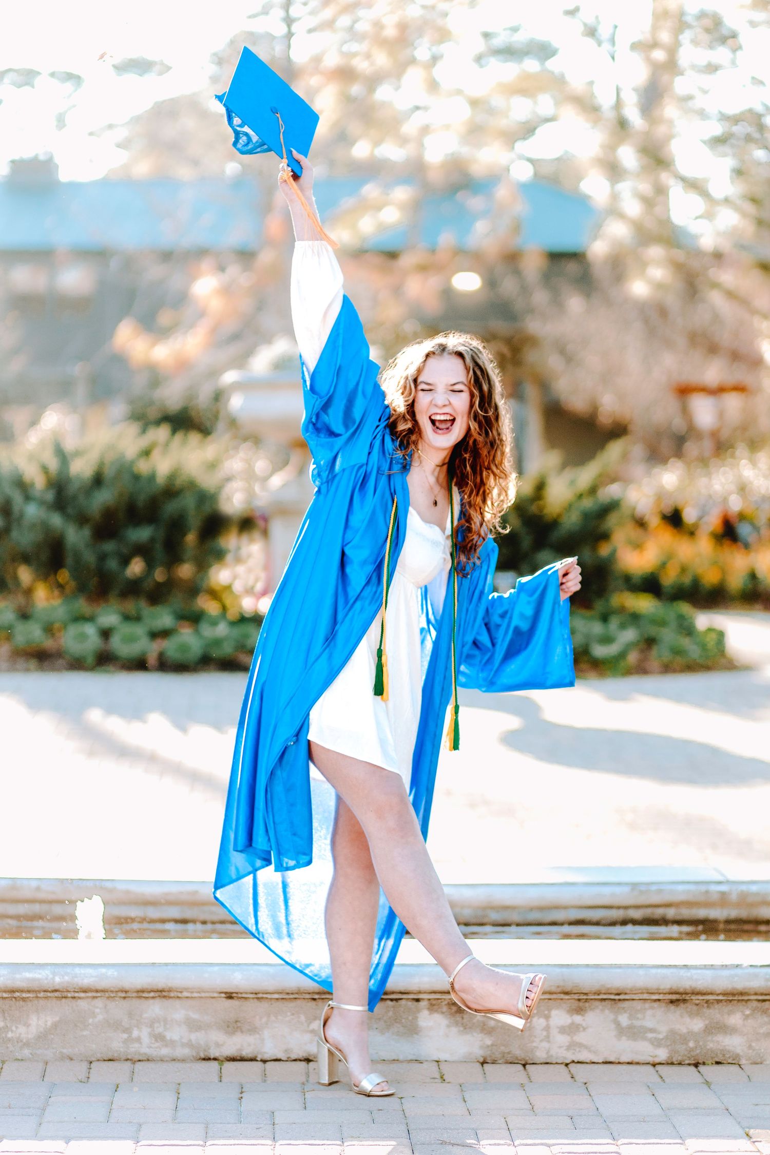 Graduate in blue cap and gown jumping for joy while celebrating outdoors on graduation day.