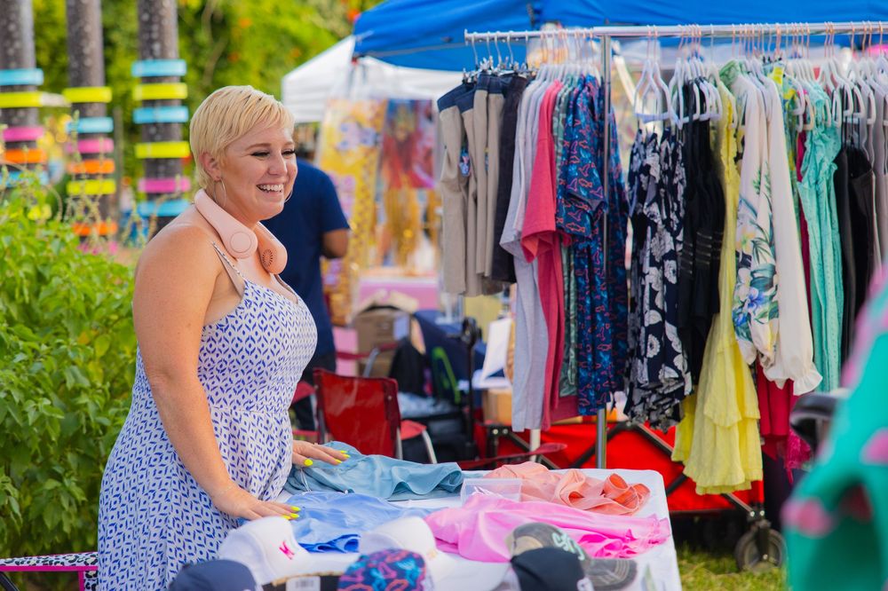 Vendor selling colorful clothing and accessories at an outdoor market booth.