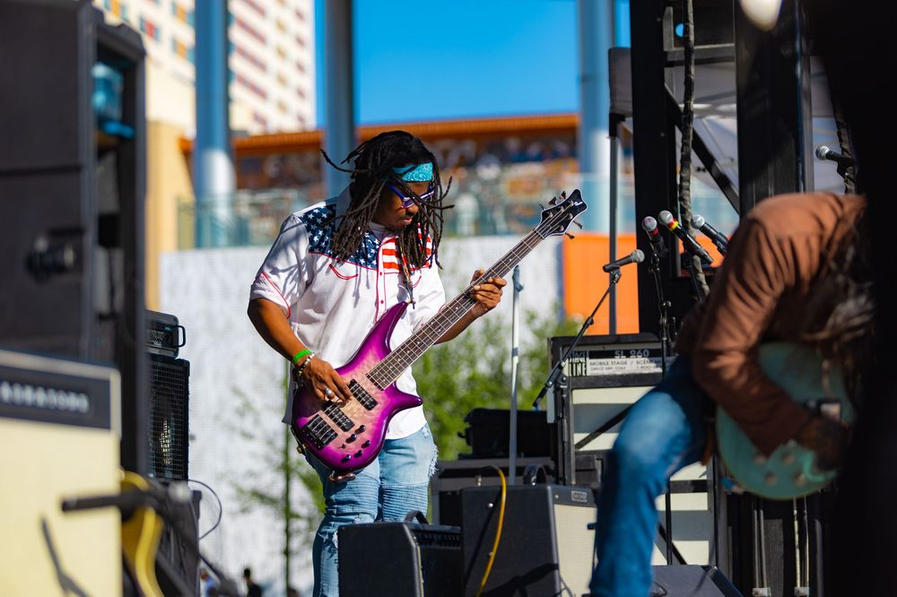 Musicians perform on stage at an outdoor event with colorful lighting and instruments.