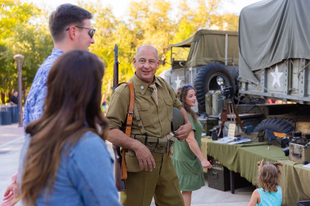 People in military uniforms gather outdoors for a community event on a sunny autumn day.
