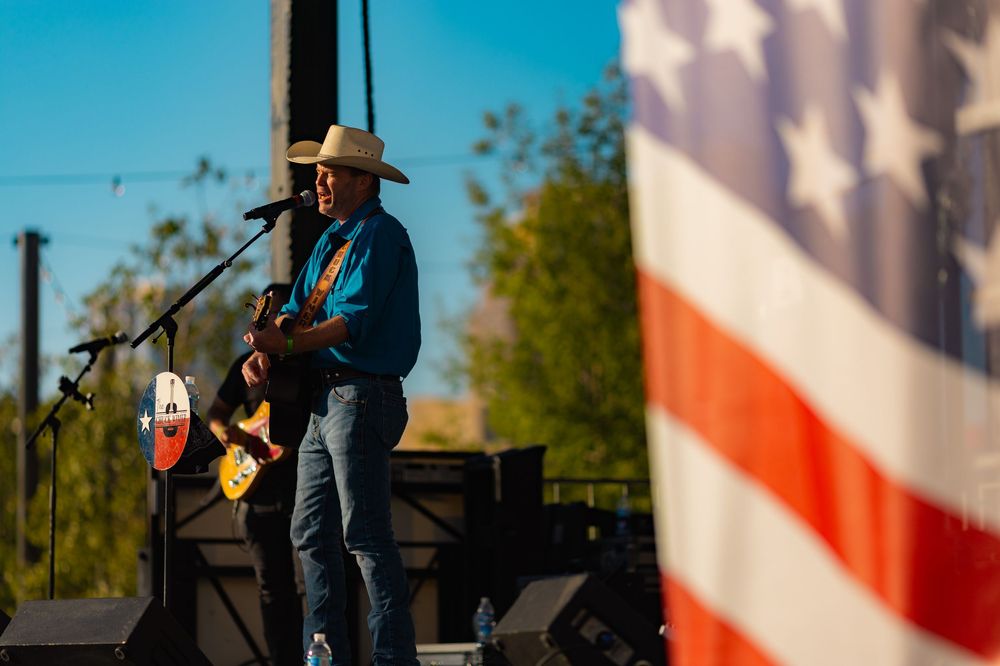 A military band performs outdoors with an American flag backdrop during a patriotic event.