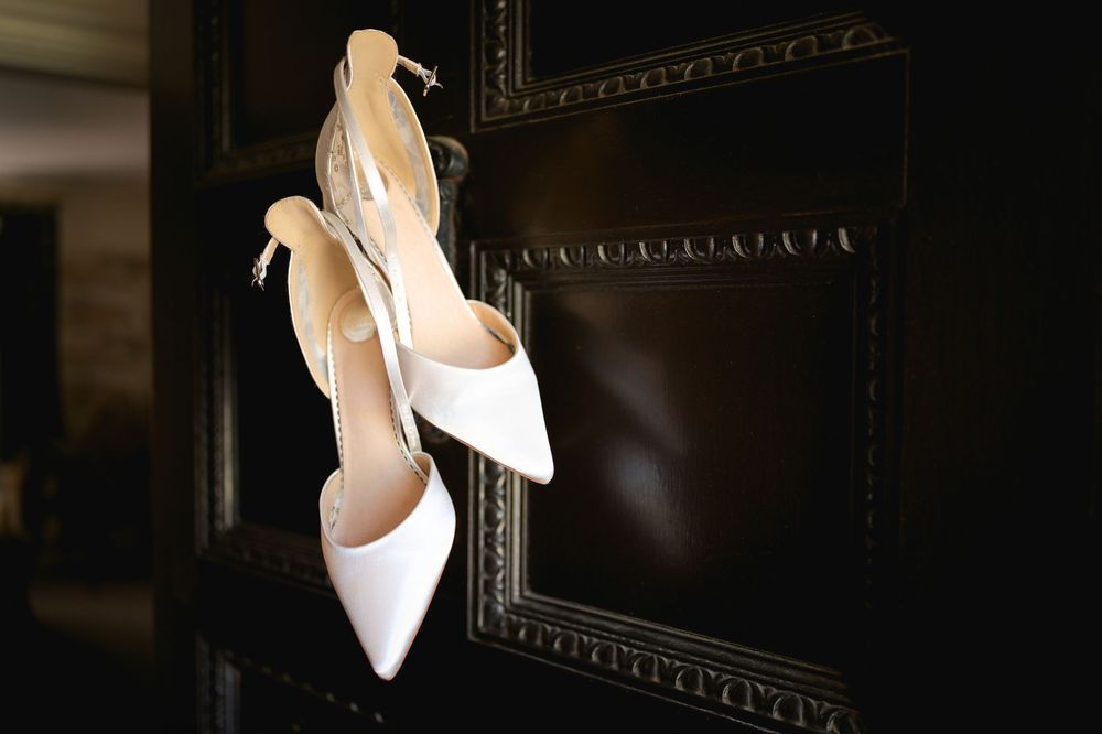 Elegant white bridal heels displayed against a dark ornate frame in dramatic lighting.